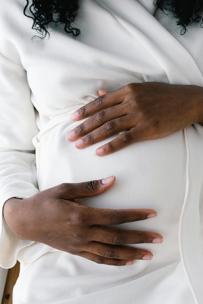 Close-up of a pregnant woman in white attire, gently touching her belly with a serene expression.